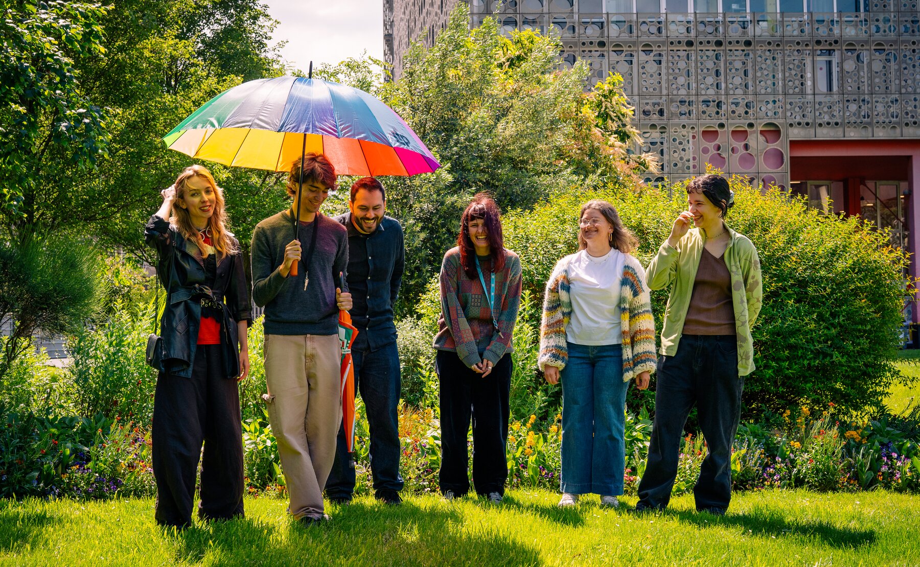 Research group outdoors under a rainbow umbrella.